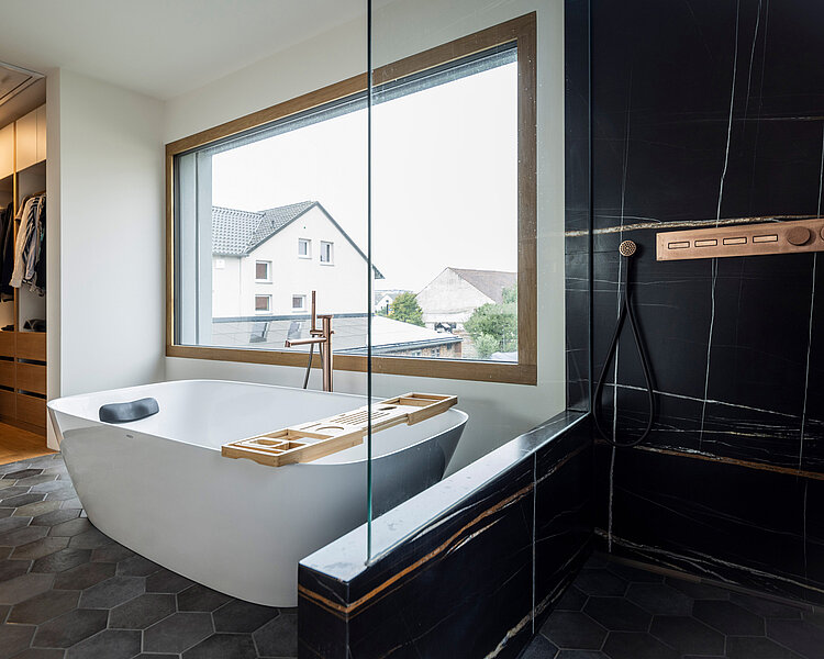 Modernes Bad mit Wanne und luxuriöser Dusche Freistehende Badewanne mit Holzablage und bodengleicher Dusche mit Kupferarmaturen in einem stilvollen Bad